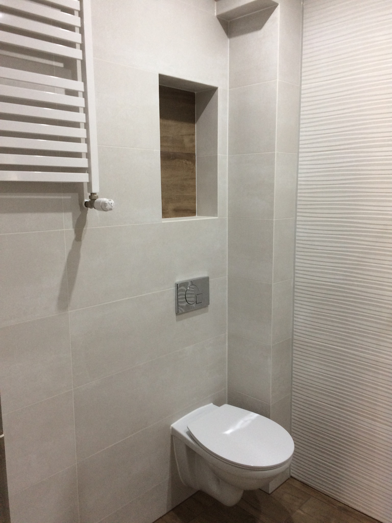 Nowoczesna łazienka z podtynkową toaletą, grzejnikiem drabinkowym i dekoracyjną wnęką z drewnianym wykończeniem.