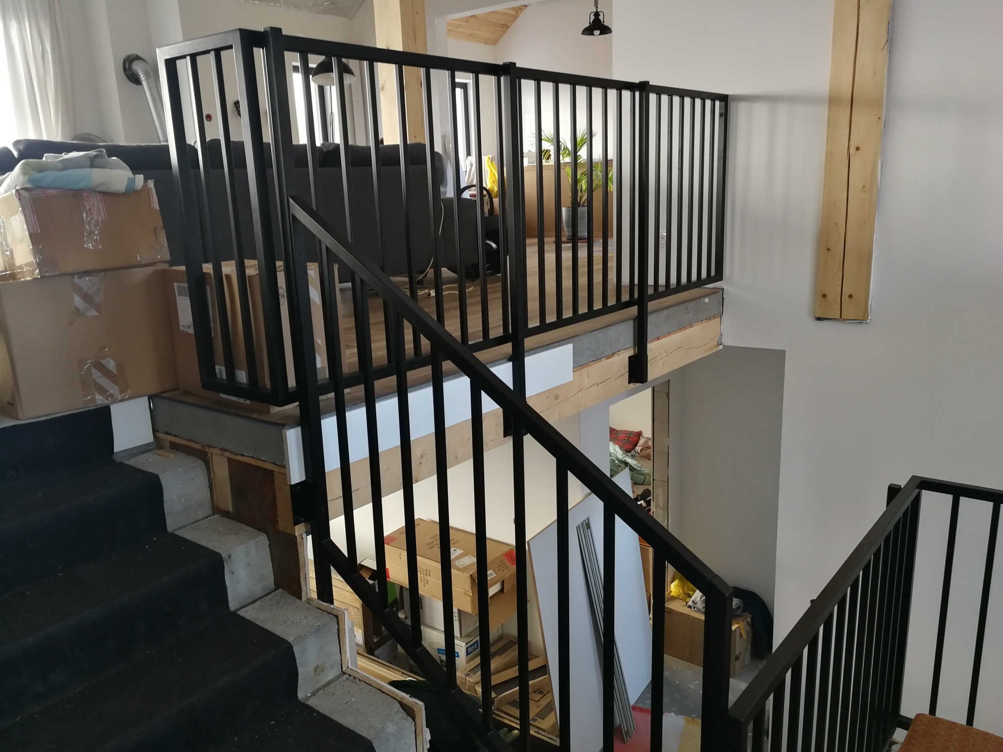 Czarne, metalowe poręcze schodowe i balustrada na antresoli w nowoczesnym wnętrzu, widok z góry na dół, częściowo widoczne kartony i inne przedmioty.