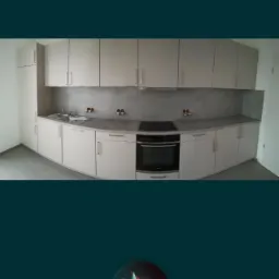 Jasna zabudowa kuchenna z szarym blatem i panelem ściennym, widoczny zlew, płyta indukcyjna i piekarnik.