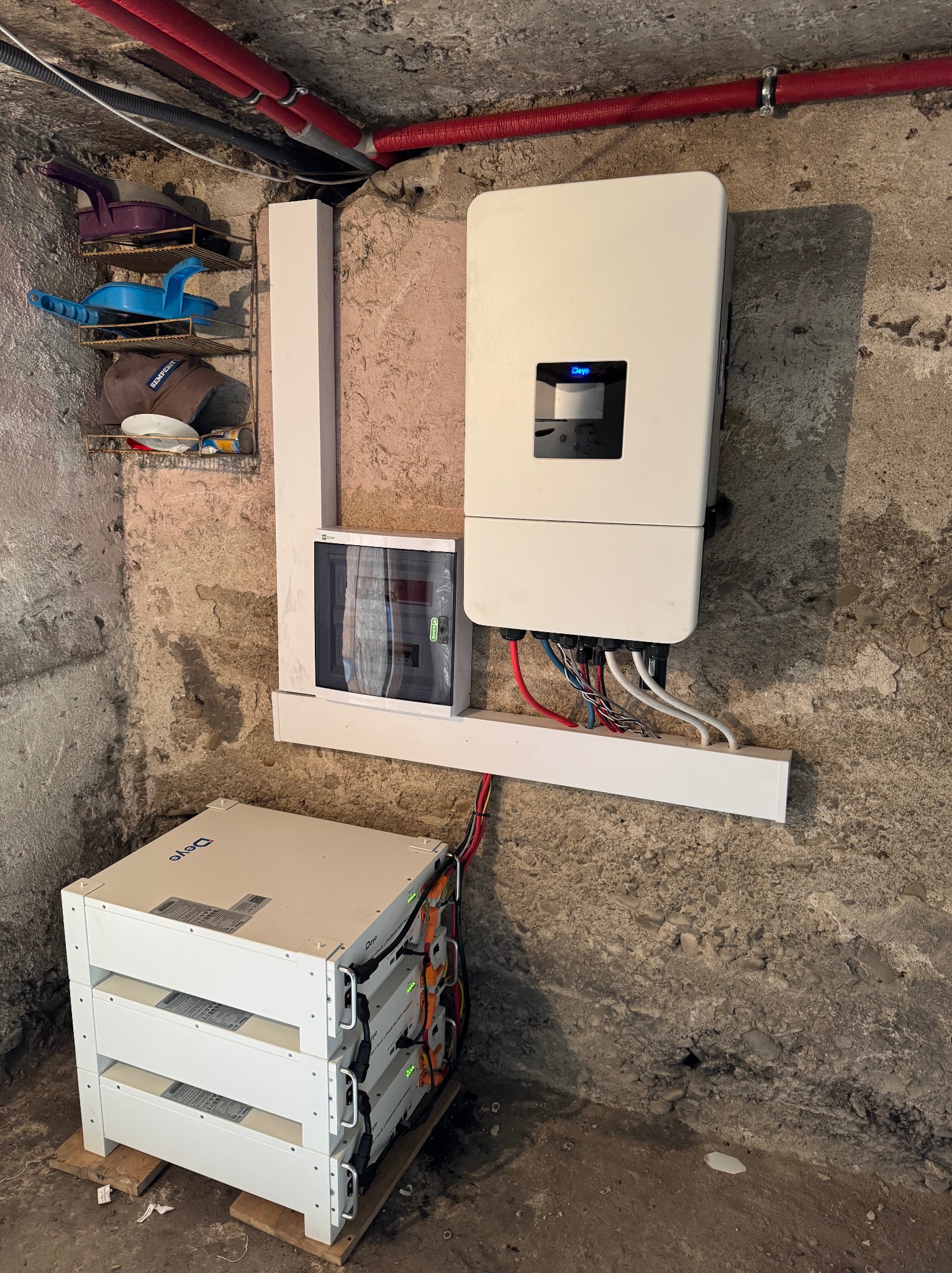 Kompletny zestaw: inwerter, rozdzielnica i moduły bateryjne magazynu energii Deye, zainstalowane w surowym pomieszczeniu z widocznymi instalacjami.