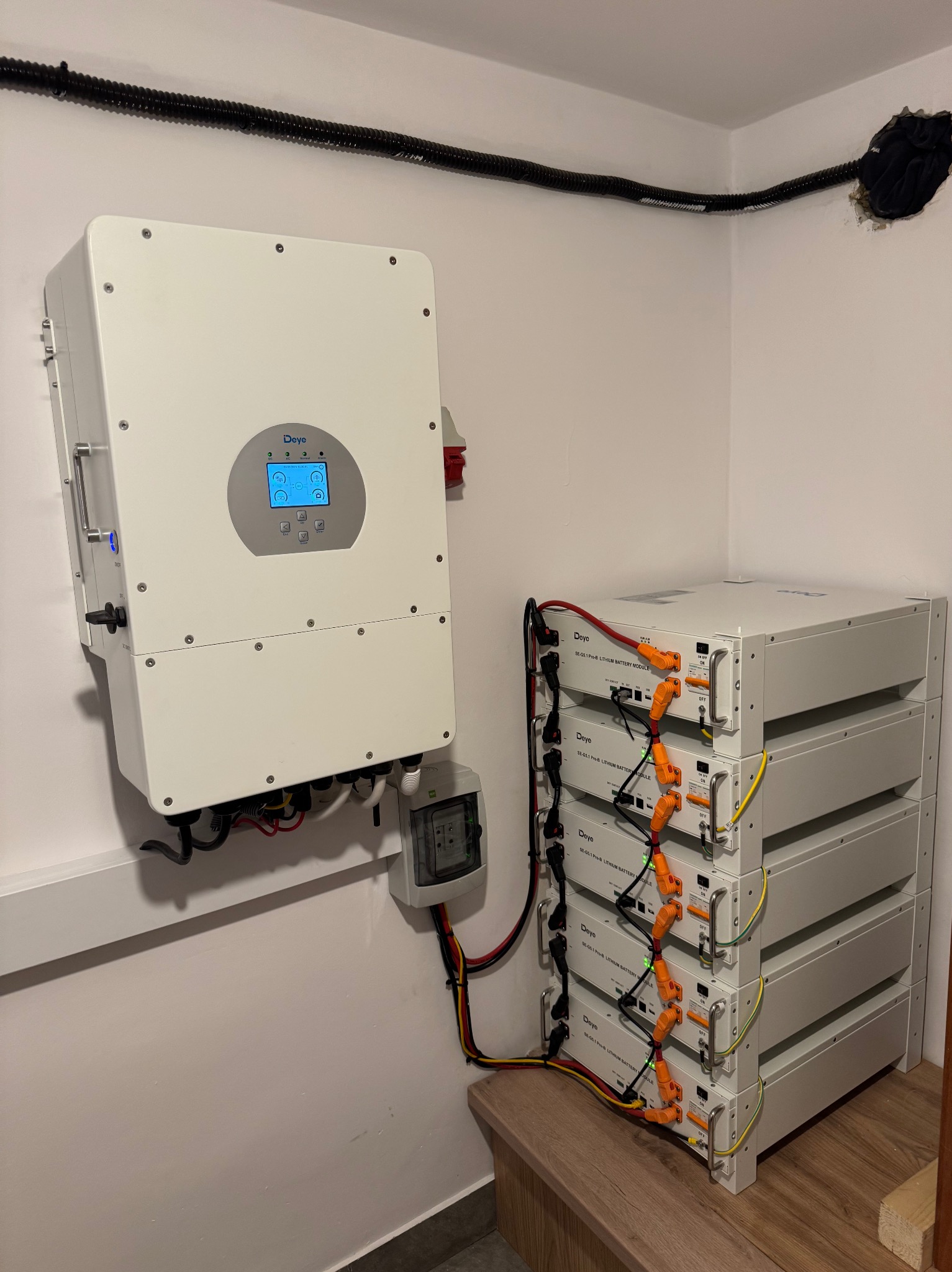 Instalacja magazynu energii Deye z falownikiem na ścianie w rogu pomieszczenia. Widoczne okablowanie i zabezpieczenia. Układ w schludnym pomieszczeniu.