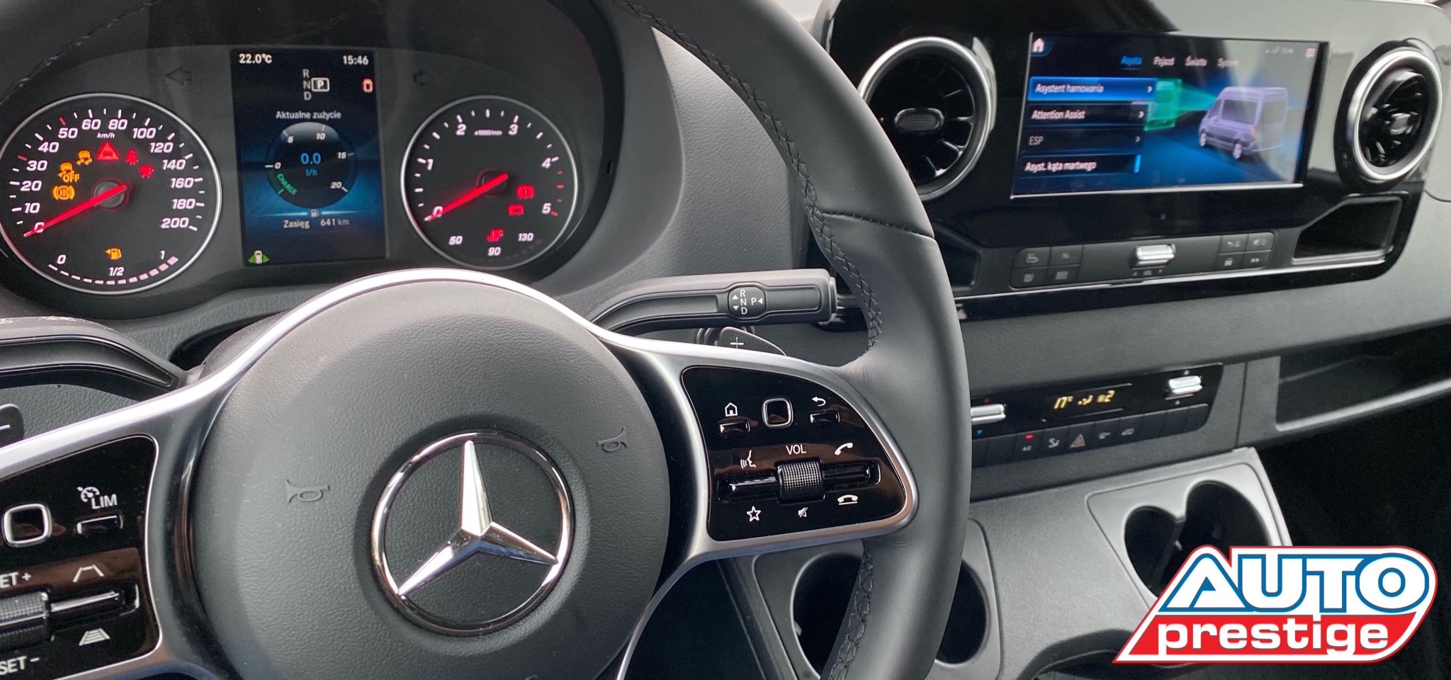 Wnętrze samochodu dostawczego Mercedes-Benz z widoczną deską rozdzielczą, kierownicą z logo Mercedes i ekranem systemu multimedialnego prezentującym funkcje asystenta hamowania, z logo firmy Auto...