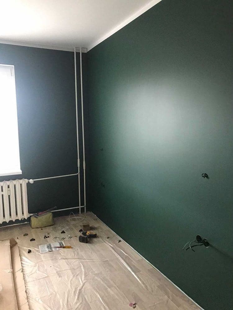 Pomieszczenie po malowaniu ścian na ciemnozielony kolor, podłoga zabezpieczona folią, widoczne narzędzia malarskie i elementy instalacji elektrycznej.