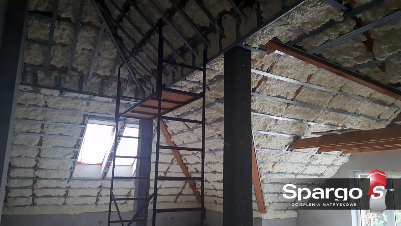 Poddasze w trakcie ocieplania pianką natryskową, widoczne metalowe profile konstrukcyjne, okno dachowe i rusztowanie.