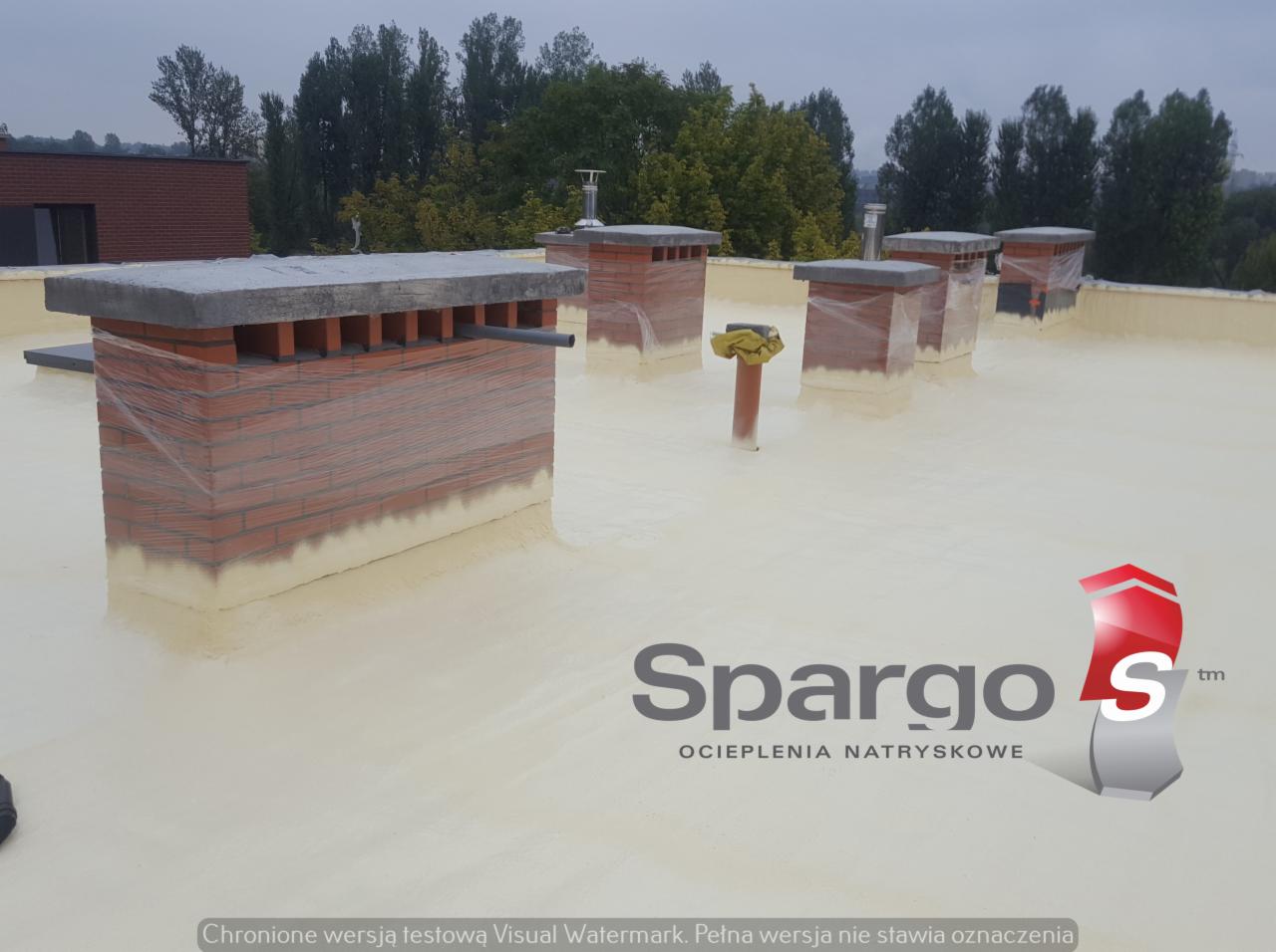 Biała pianka izolacyjna pokrywa płaski dach z kominami zabezpieczonymi folią; widoczny budynek w tle i logo firmy.