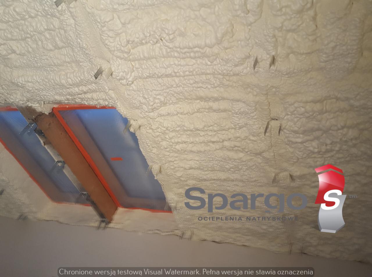Poddasze ocieplone pianką PUR z widocznym oknem dachowym i drewnianą konstrukcją, z logo firmy Spargo's Ocieplenia Natryskowe w prawym dolnym rogu.