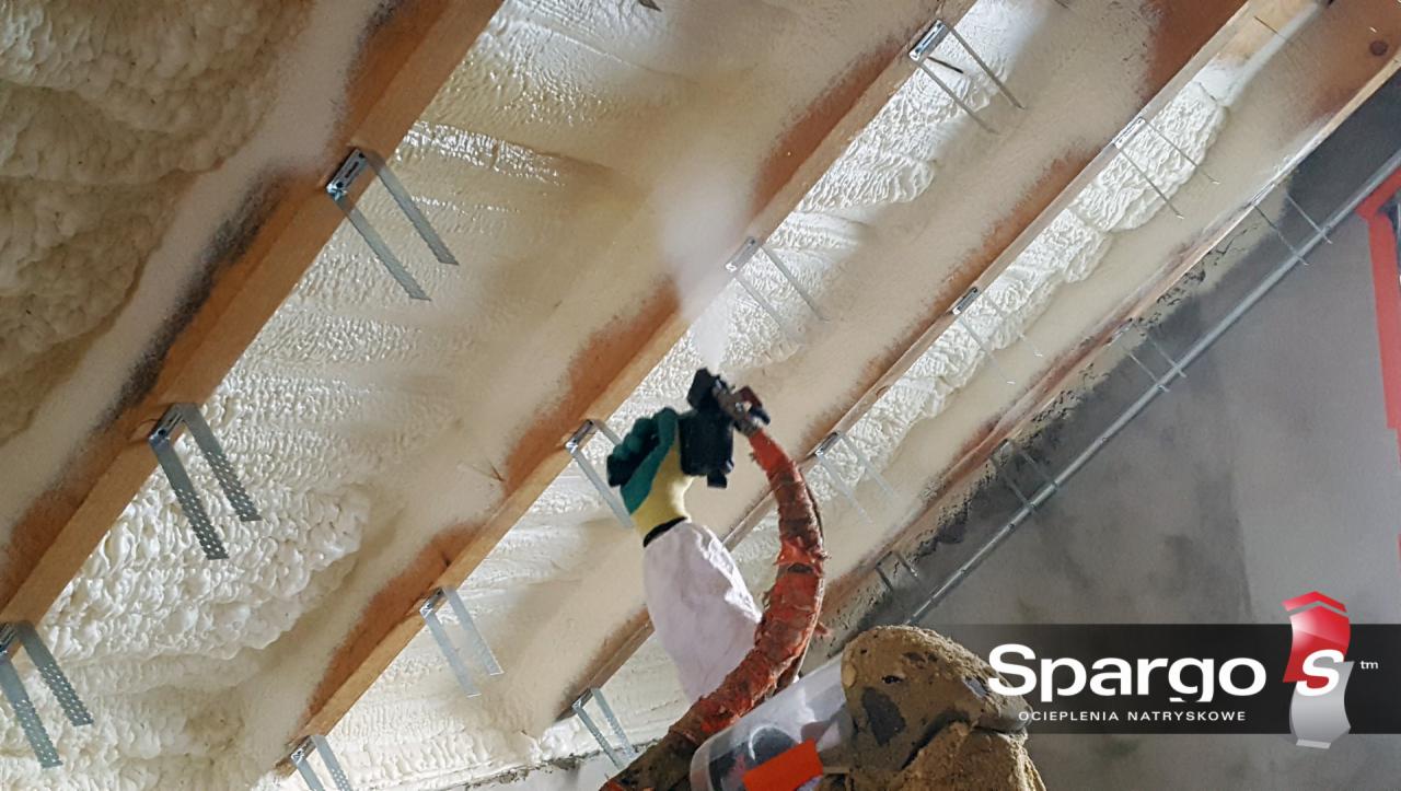 Prace związane z natryskiem izolacji piankowej na poddaszu w Niegowie, widoczny aplikator i fragment ocieplonej powierzchni z elementami konstrukcji dachu.