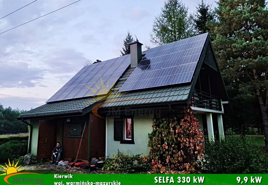 Instalacja paneli słonecznych Selfa 330W o mocy 9,9 kW na dachu domu jednorodzinnego z zielonym dachem w województwie warmińsko-mazurskim, widok z poziomu gruntu, na pierwszym planie siedząca osoba...