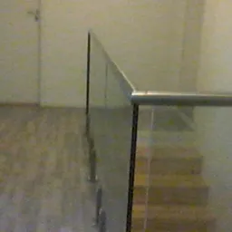 Szklana balustrada schodowa z metalowym poręczą w jasnym wnętrzu, widok z góry na drewniane stopnie.