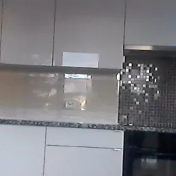 Nowoczesna kuchnia z białymi szafkami, blatem z szarego granitu i mozaiką nad blatem, widoczny fragment piekarnika