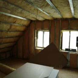 Poddasze w trakcie ocieplania wełną mineralną, widoczne metalowe profile konstrukcyjne, dwie pary okien dachowych i płyty gipsowo-kartonowe przygotowane do montażu.