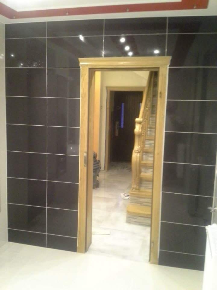 Wykończona łazienka z czarnymi płytkami na ścianach, widok na korytarz przez drewnianą futrynę drzwiową, biała podłoga.