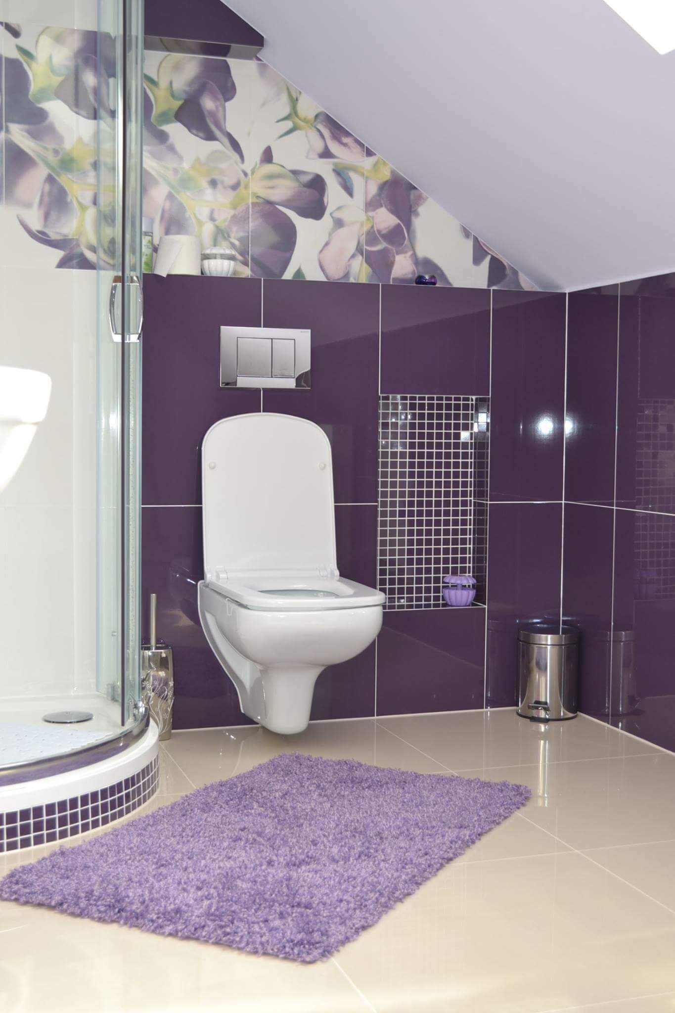 Fioletowa łazienka na poddaszu z kabiną prysznicową, toaletą i fioletowym dywanikiem.