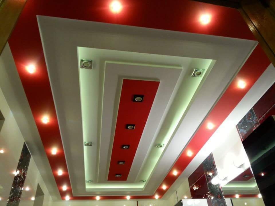 Wielopoziomowy sufit podwieszany z czerwonymi akcentami i oświetleniem punktowym, widok z dołu.