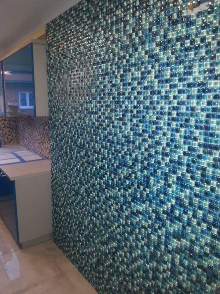 Ściana w kuchni wyłożona mozaiką z małych, kwadratowych płytek w odcieniach błękitu i szarości, sąsiadująca z białymi szafkami kuchennymi i blatem.