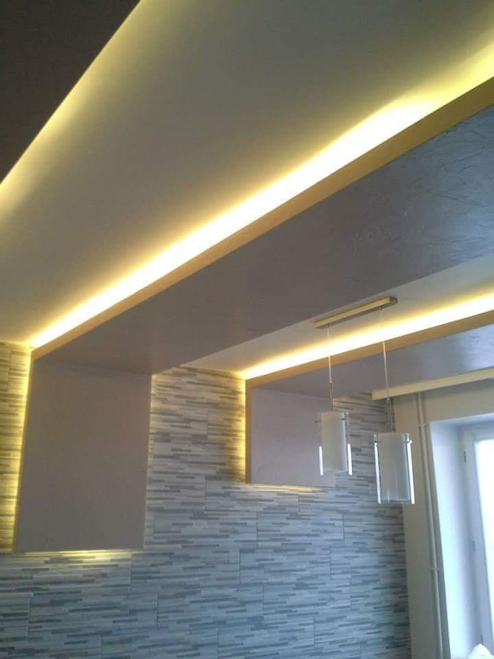 Nowoczesny sufit podwieszany z oświetleniem LED i dekoracyjna ściana z płytek imitujących drewno w odcieniach szarości, wiszące lampy tuby, widok z dołu.