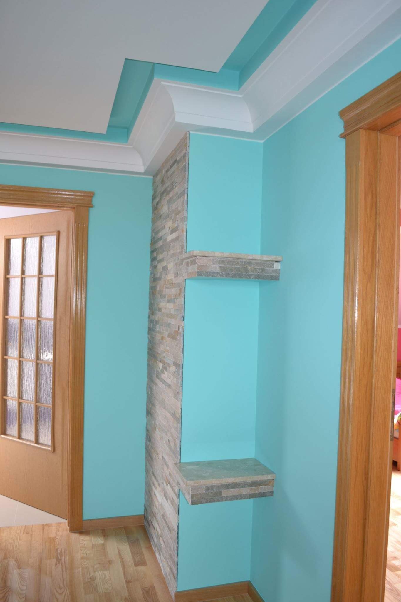 Turkusowe ściany z dekoracyjną ścianką z kamienia i półkami, drewniana stolarka drzwiowa, listwy sufitowe w dwóch kolorach.