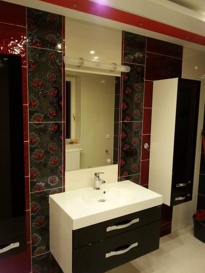 Nowoczesna łazienka z umywalką na szafce w kolorze czarno-białym, lustrem z oświetleniem i dekoracyjnymi płytkami w odcieniach czerwieni, czerni i bieli.