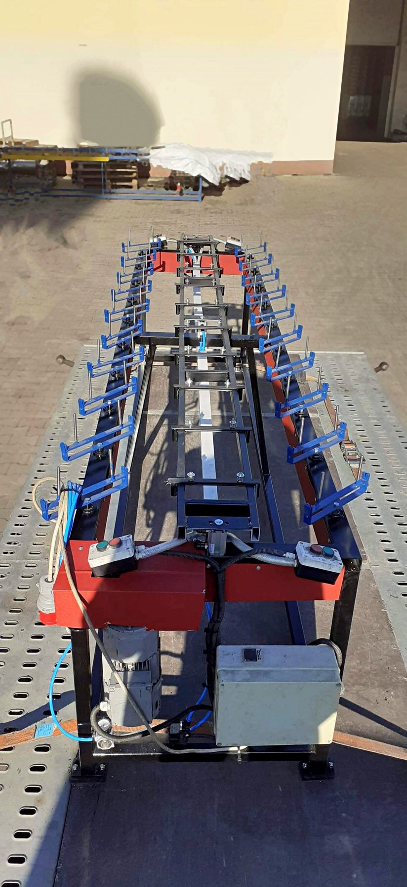 Stół spawalniczy z pneumatycznymi zaciskami, widoczne silniki i przewody pneumatyczne, ujęcie z góry na zewnątrz.