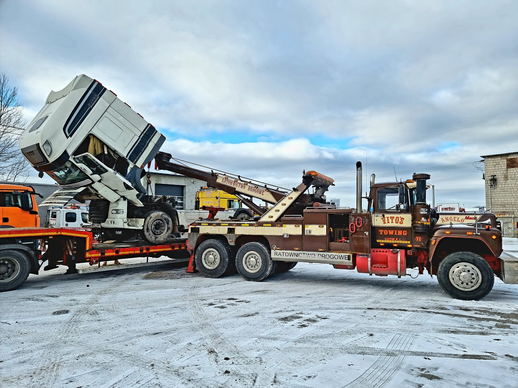 Uszkodzona kabina ciężarówki DAF Super Space Cab, uniesiona przez ramię lawety z napisem 'Ratownictwo Drogowe', w zimowych warunkach.