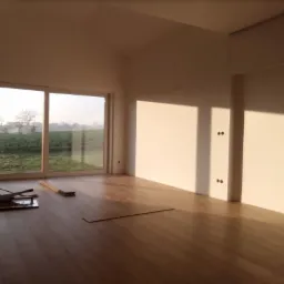 Montaż parkietu w jasnym pokoju z dużym oknem na ogród, widoczne narzędzia i deski podłogowe, popołudniowe światło podkreśla strukturę drewna.