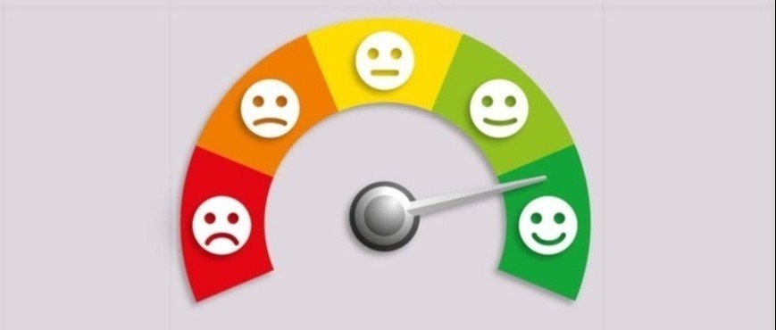 Miernik satysfakcji klienta z podziałem na strefy kolorystyczne (czerwona - niezadowolenie, żółta - neutralność, zielona - zadowolenie) i emotikony wyrażające różne nastroje, wskazówka ustawiona...