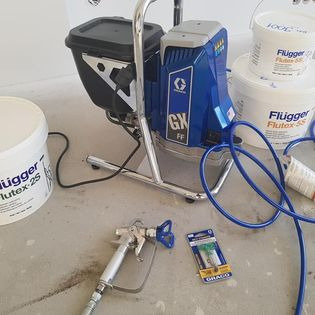 Agregat malarski Graco GX FF z akcesoriami i farbami Flugger Flutex 2S i Flutex-2S, przygotowany do pracy na jasnej posadzce.