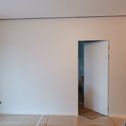 Repasbud - Przygotowanie do malowania ścian: zabezpieczona folią podłoga, obklejone taśmą malarską listwy i narożniki, widoczne gniazdka elektryczne i otwarta biała ściana.