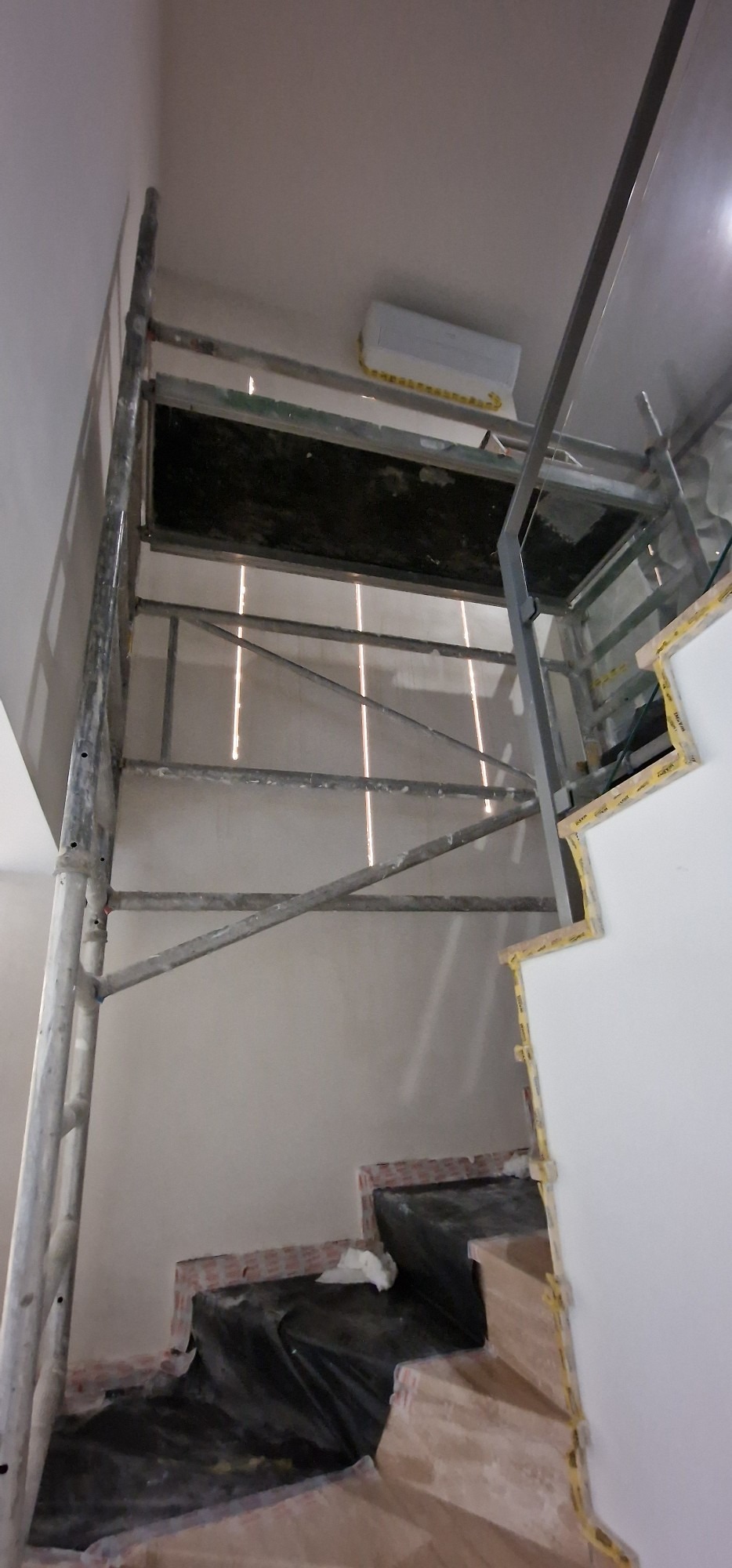 Metalowe rusztowanie ustawione przy ścianie w trakcie remontu, widoczne zabezpieczone schody i klimatyzator na suficie.