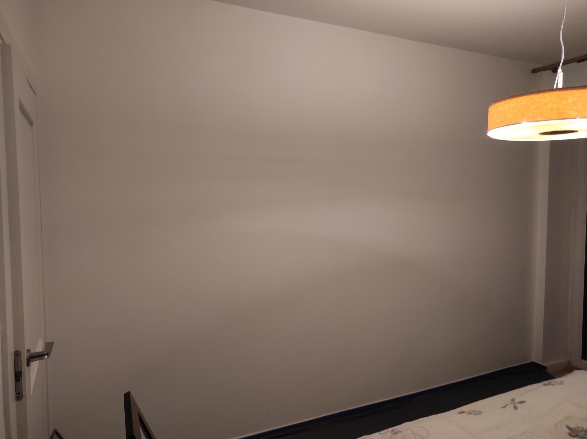 Świeżo pomalowana, gładka ściana w pokoju z widocznym fragmentem osłony podłogi i lampą sufitową w ciepłych odcieniach.