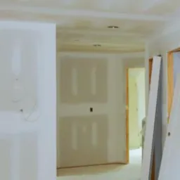 Wnętrze w trakcie prac wykończeniowych: ściany pokryte płytami kartonowo-gipsowymi, sufit z zamontowanymi punktami oświetleniowymi, widoczne ościeżnice drzwiowe.