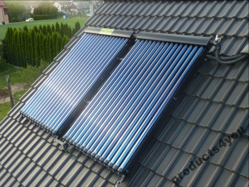 Dwa panele słoneczne rurowe marki AK LUX zamontowane na ciemnoszarym dachu z dachówki ceramicznej, widok z góry na tle zielonych drzew.