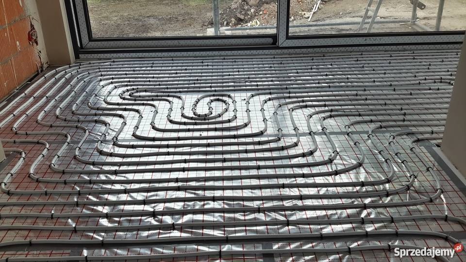 Rozłożone rury ogrzewania podłogowego na folii izolacyjnej z siatką, widok z góry na przygotowany system przed wylaniem wylewki.