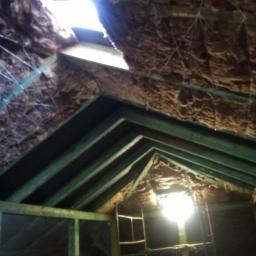 FHU Nikiel Maciej - Poddasze w trakcie prac izolacyjnych, widoczne drewniane krokwie, ocieplenie wełną mineralną oraz rusztowanie. W tle prześwituje światło dzienne przez otwór w dachu.