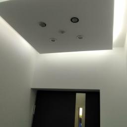 FHU Nikiel Maciej - Nowoczesny sufit podwieszany z oświetleniem LED i czterema punktami świetlnymi, widok z dołu na tle ściany i drzwi.