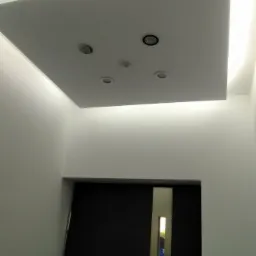 Nowoczesny sufit podwieszany z oświetleniem LED i czterema punktami świetlnymi, widok z dołu na tle ściany i drzwi.