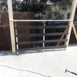 Luk-Spaw - Montaż zewnętrznej konstrukcji z poziomych, czarnych listew i stalowej rurki, widoczne narzędzia pracy i elementy mocujące.