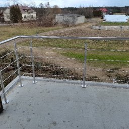 Luk-Spaw - Balkon z balustradą nierdzewną o minimalistycznym designie, widok na wiejski krajobraz z domami i polami w tle.