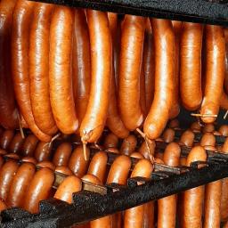 Firma Tołłoczko - Wędzone kiełbasy ułożone rzędami na czarnym, metalowym stojaku, gotowe do sprzedaży.