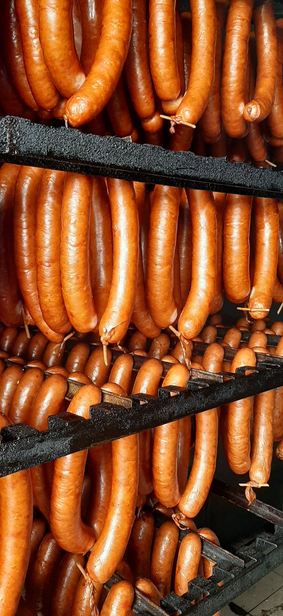 Wędzone kiełbasy ułożone rzędami na czarnym, metalowym stojaku, gotowe do sprzedaży.