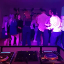 Dj Numark przy konsolecie podczas imprezy w fioletowym oświetleniu, w tle tańczący goście i balon w kształcie cyfry 18.