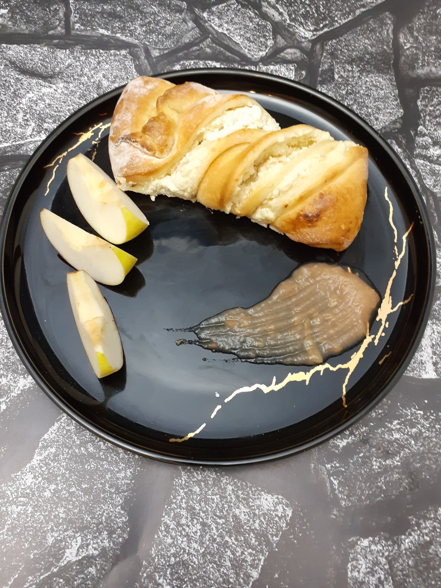 Twarożnica, trzy plasterki jabłka i mus owocowy na czarnym talerzu ze złotymi zdobieniami, na tle imitującym kamień.