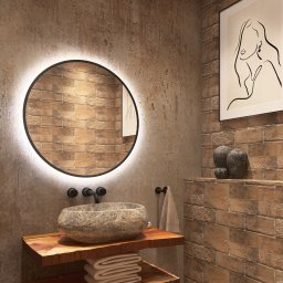 Aleksandra Plucińska - Nowoczesna łazienka z okrągłym lustrem LED, kamienną umywalką na drewnianym blacie i ceglaną ścianą. Dwa obrazy w czarnych ramach dodają elegancji.