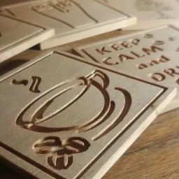 Drewniane podkładki z wygrawerowanymi wzorami: filiżanka kawy, napis 'Keep Calm and Drink Coffee', szyszka chmielu i drzewo.
