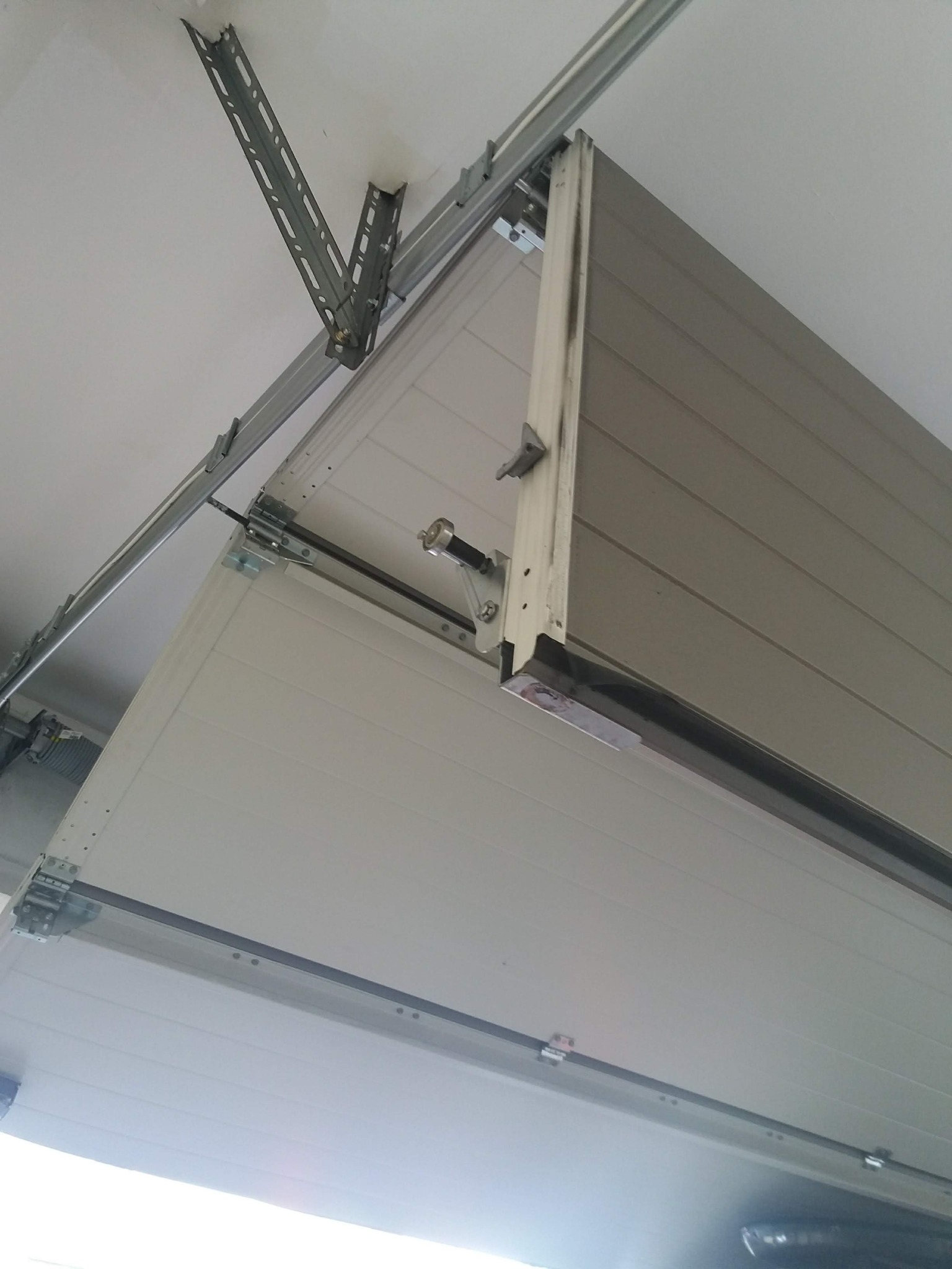 Widok od dołu na zamontowaną segmentową bramę garażową z widocznymi prowadnicami i mechanizmem sprężynowym.