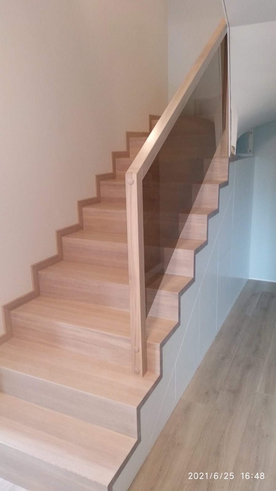 Jasne, drewniane stopnie schodów z przeszkloną balustradą, widok z dołu, minimalistyczny design.