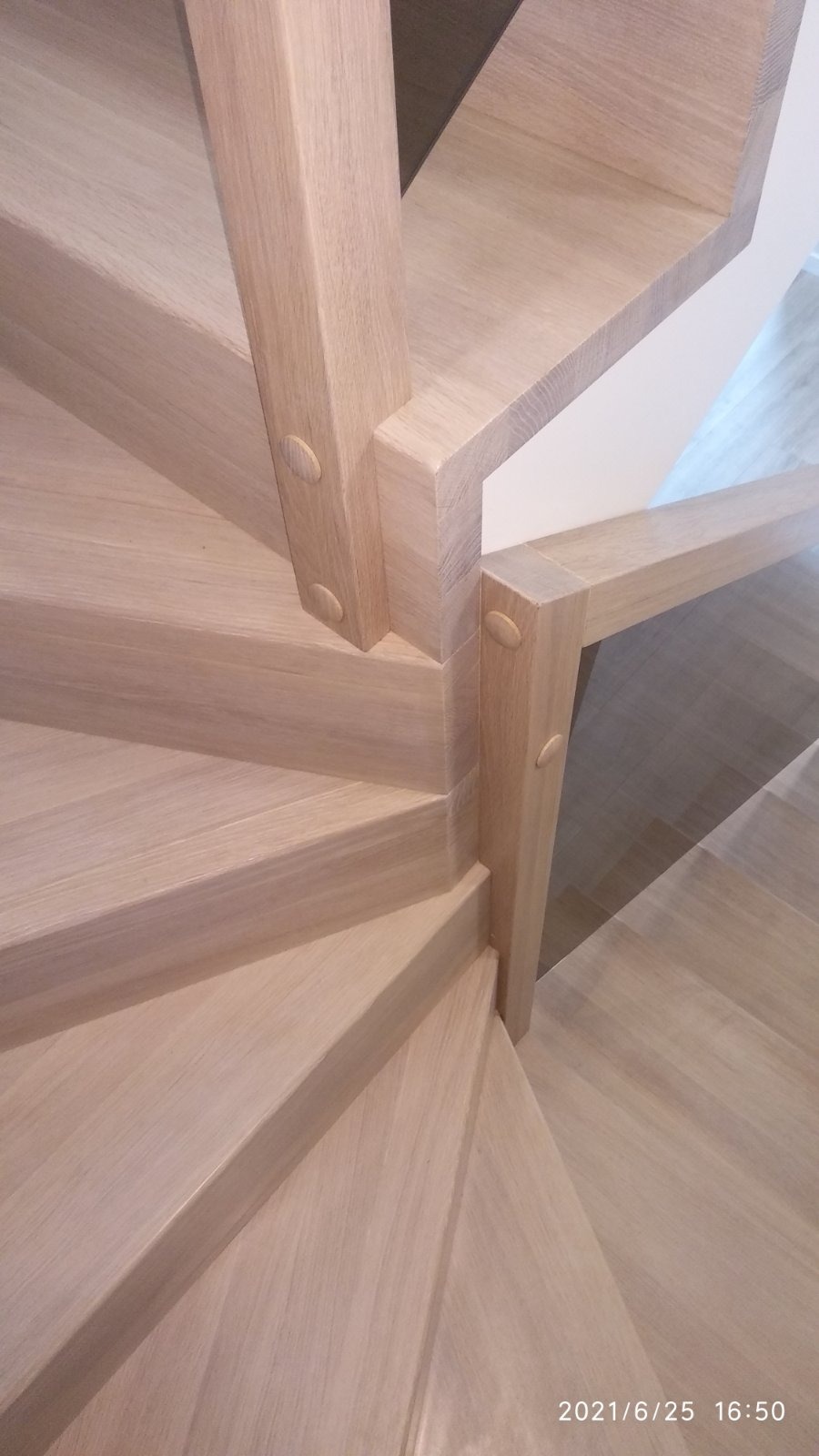 Spiralne, jasne, dębowe stopnie z widocznymi drewnianymi kołkami mocującymi poręcz, ujęcie z góry.