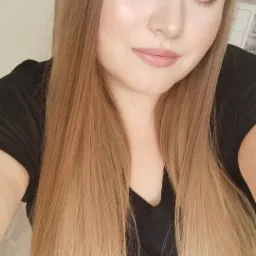 Portret młodej kobiety z długimi, blond włosami z ombre, delikatny makijaż z czarną kreską na powiece, na tle białych drzwi.