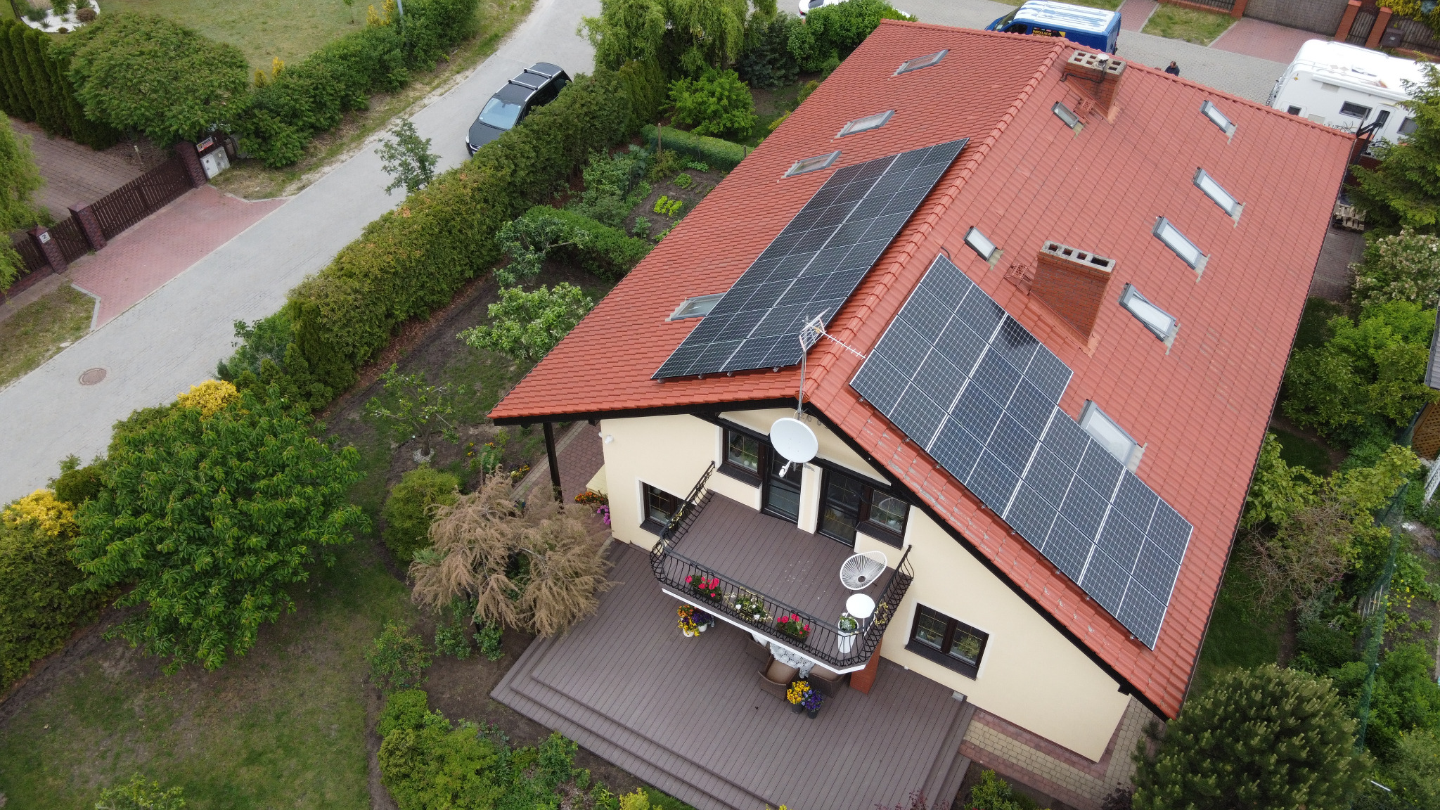 Widok z drona na dom z czerwoną dachówką i panelami słonecznymi, Niemcz. Na balkonie kwiaty, obok zadbany ogród.