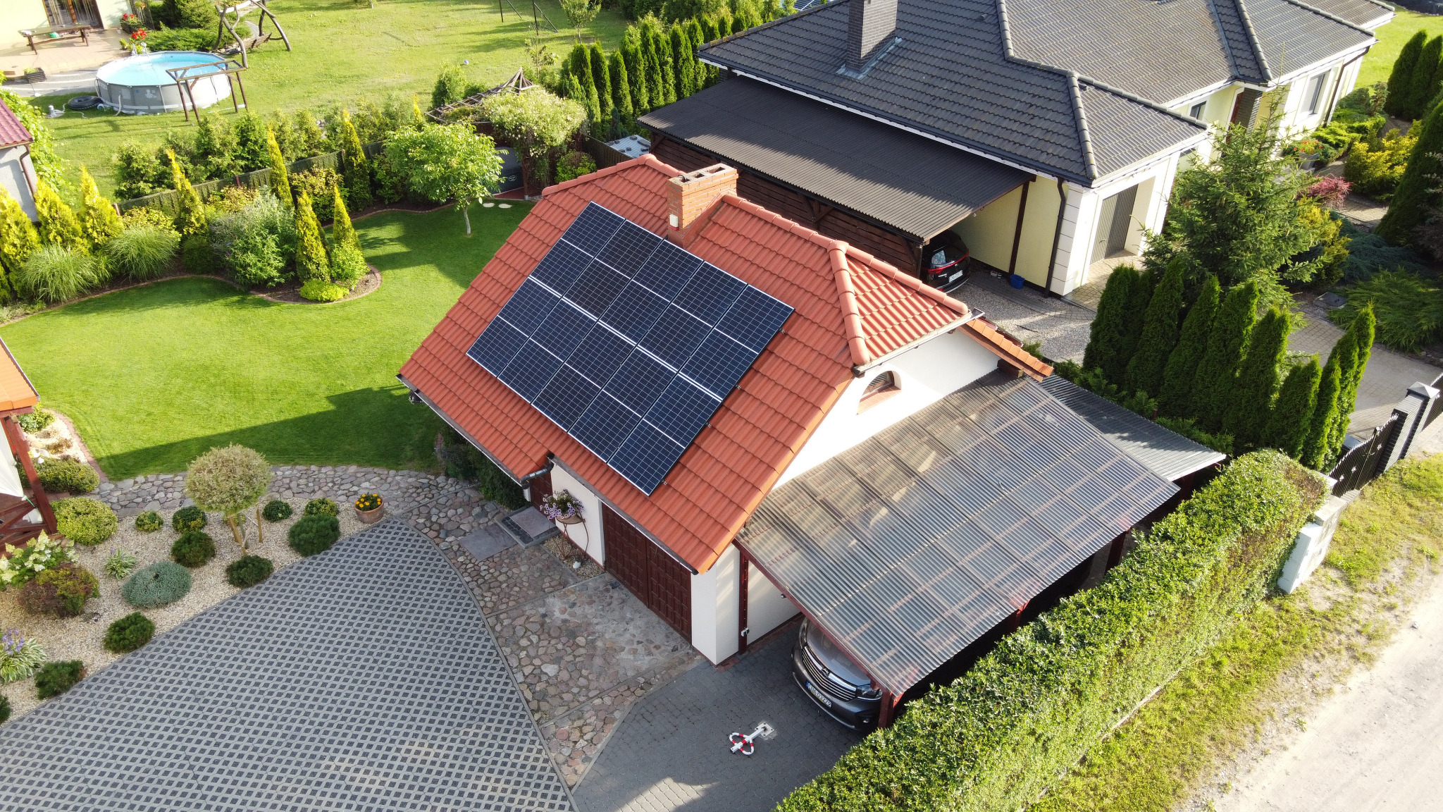 Widok z drona na dom jednorodzinny w Szubinie z panelami słonecznymi na czerwonym dachu i zadaszeniem nad miejscem parkingowym.